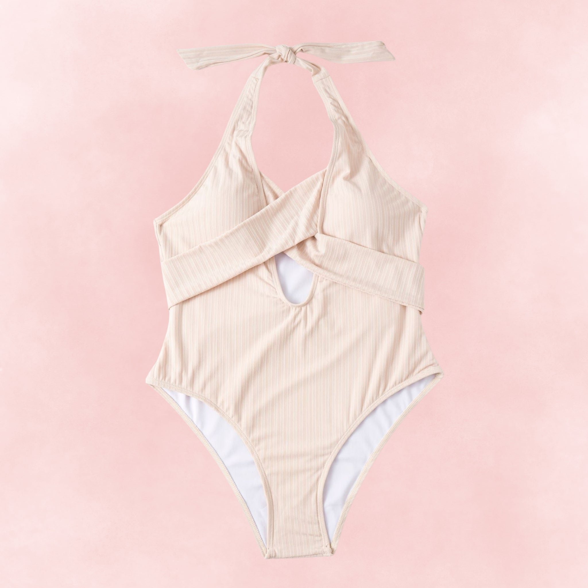 Flat lay of plus size beige ribbed one-piece swimsuit with crisscross halter straps and cutout front