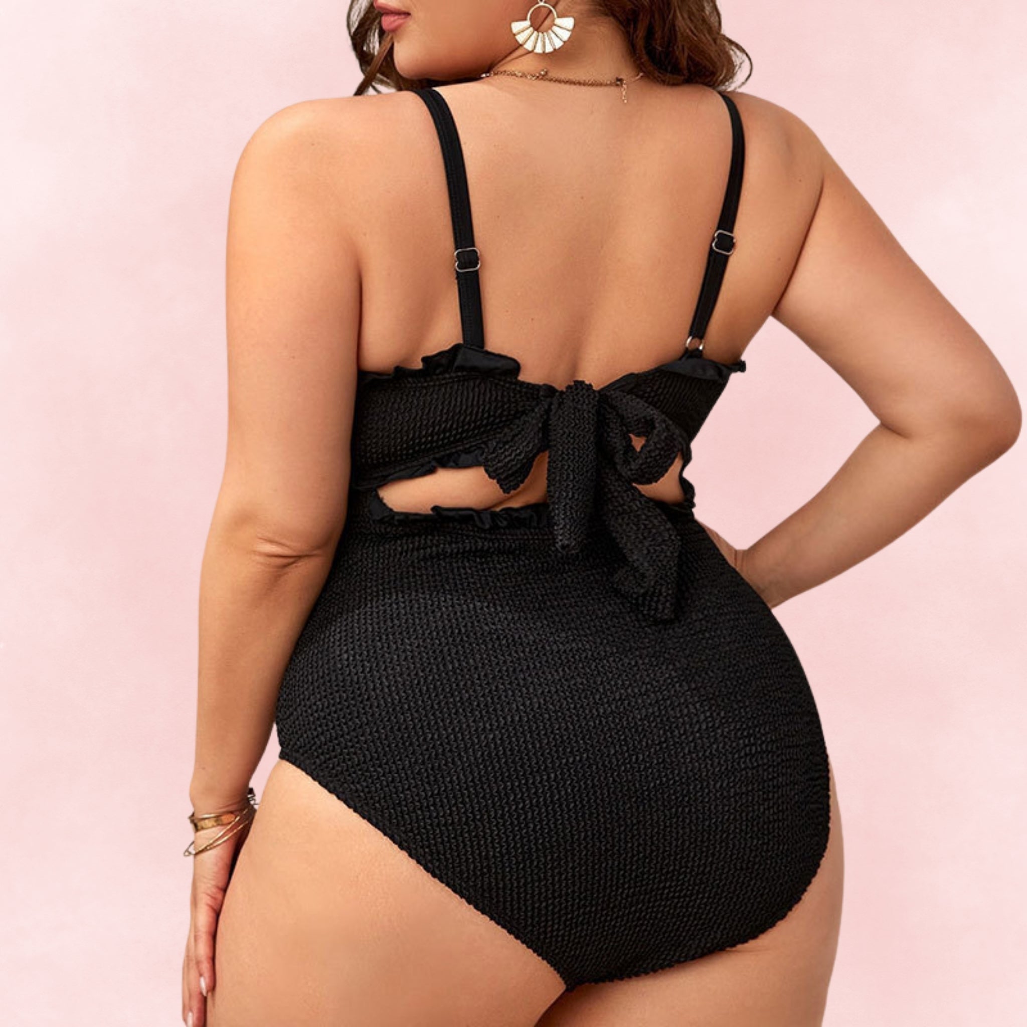 Back view of plus size black smocked one-piece swimsuit with tie-back bow and ruffle trim